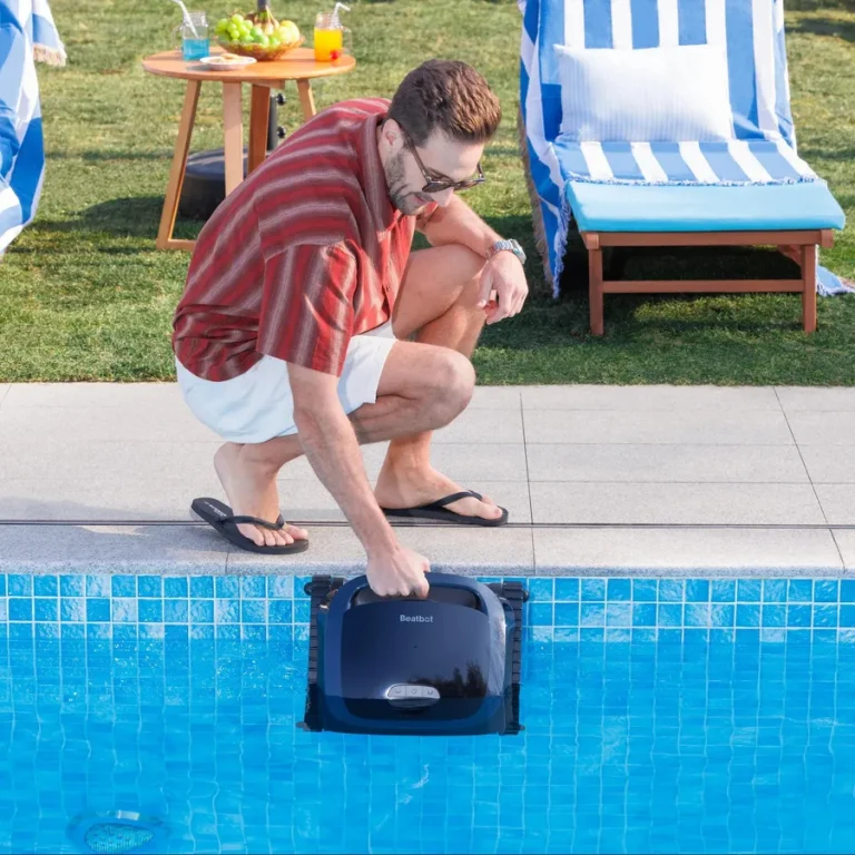 Man vid poolkanten sänker ner en poolrobot i vattnet